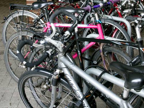 Eine Reihe von Anlehnbügeln für Fahrräder, jeder Stellplatz ist von einem Fahrrad besetzt. Es sind viele verschiedene Modelle in verschiedenen Farben zu sehen.